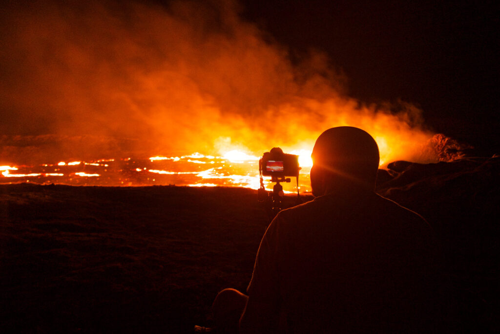 a person next to a camera on a tripod on the edge of the volcano at night.